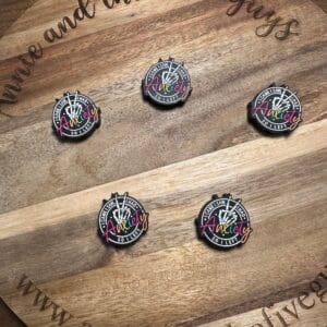 Five commemorative pins with "celebrating 10 years" and "AnnieLy" text displayed on a wooden board with "Annie and the Five Guys" and "www.annieandthefiveguys.com" text around the edge are replaced by Your anxiety is a lying hoe silicone focal bead.