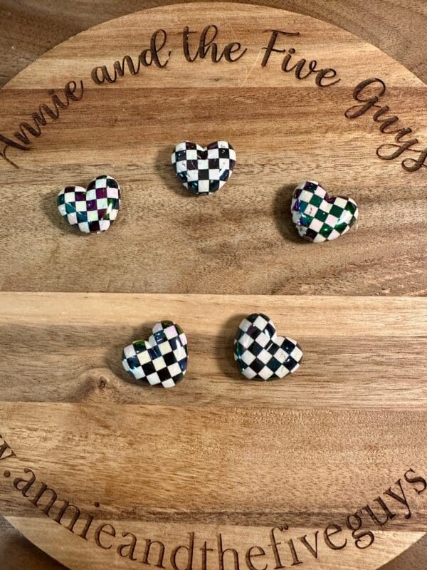 Five checkered heart beads are placed on a wooden board with the text "Annie and the Five Guys" engraved around the edge.