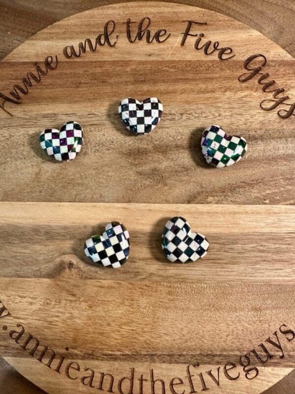 Five checkered heart beads are placed on a wooden board with the text "Annie and the Five Guys" engraved around the edge.