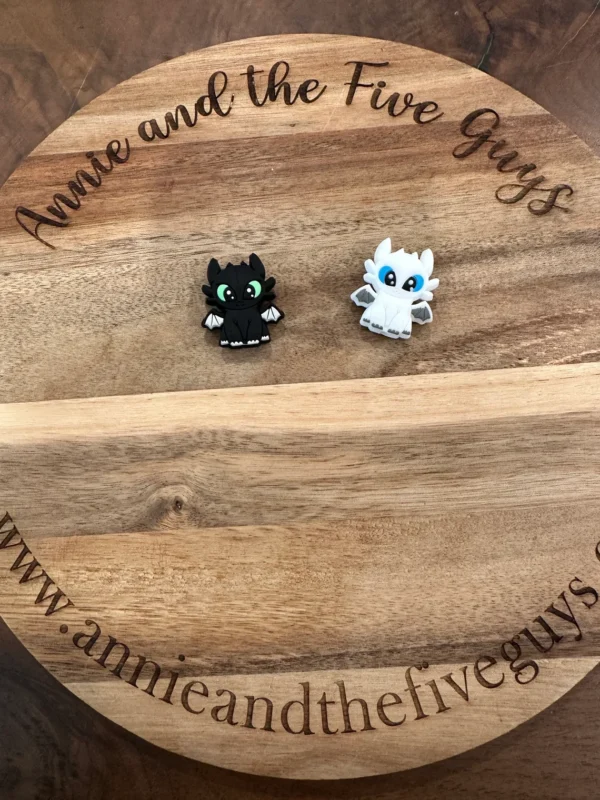 Two small Dragon figurines, one black and one white, are placed on a round wooden board with the text "Annie and the Five Guys" engraved around the edge.