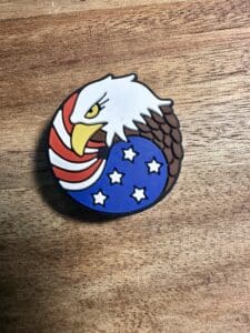 A silicone focal bead featuring an eagle with a white head, yellow beak, and brown feathers, overlaid with the American flag's red and white stripes and blue field with white stars.