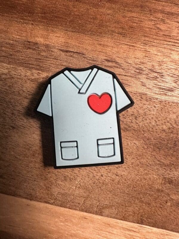 A Stethoscope silicone focal bead shaped like a medical scrub top with a heart on the chest is placed on a wooden surface.