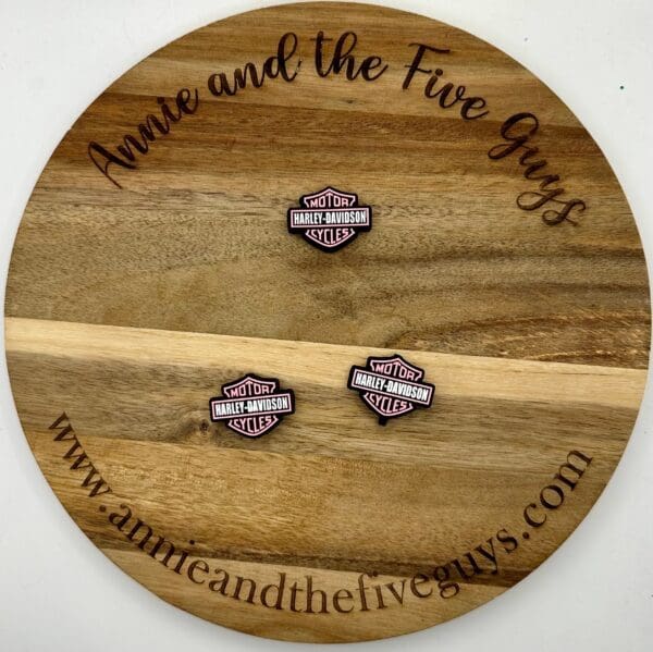 A round wooden board featuring the text "Annie and the Five Guys" with a motorcycle focal bead placed on it. The website "www.annieandthefiveguys.com" is also visible on the board.