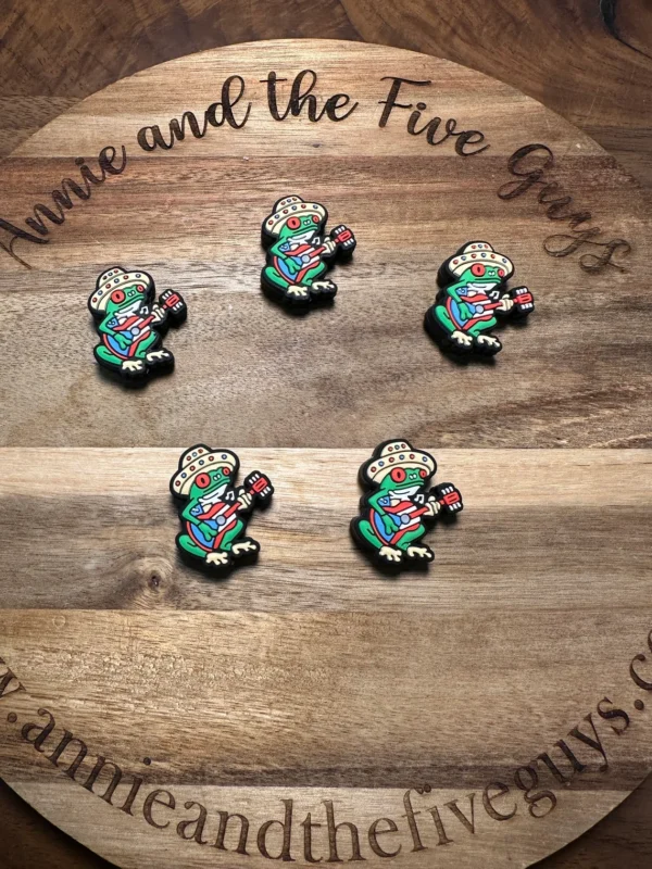 Five Puerto Rican coquí silicone focal beads featuring a frog playing an electric guitar on a wooden surface with the text "Annie and the Five Guys" and a website URL.