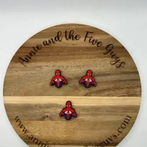 A round wooden board with the text "Annie and the Five Guys" features three small Spider guy focal beads. The website "www.annieandthefiveguys.com" is also printed on the board's rim.