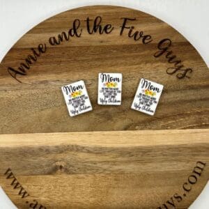 A round wooden board with the words "Annie and the Five Guys" and the website "www.annieandthefiveguys.com," displaying three small Mom silicone focal beads.