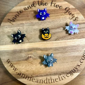 Small 3D bat or pumpkin cat silicone focal beads are arranged in a circle on a wooden display board with the text "Annie and the Five Guys" and the website "www.annieandthefiveguys.com".