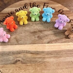 Six Bear furry looking acrylic beads in various colors (orange, pink, yellow, green, blue, purple, brown) are displayed on a wooden surface with text partially visible above.