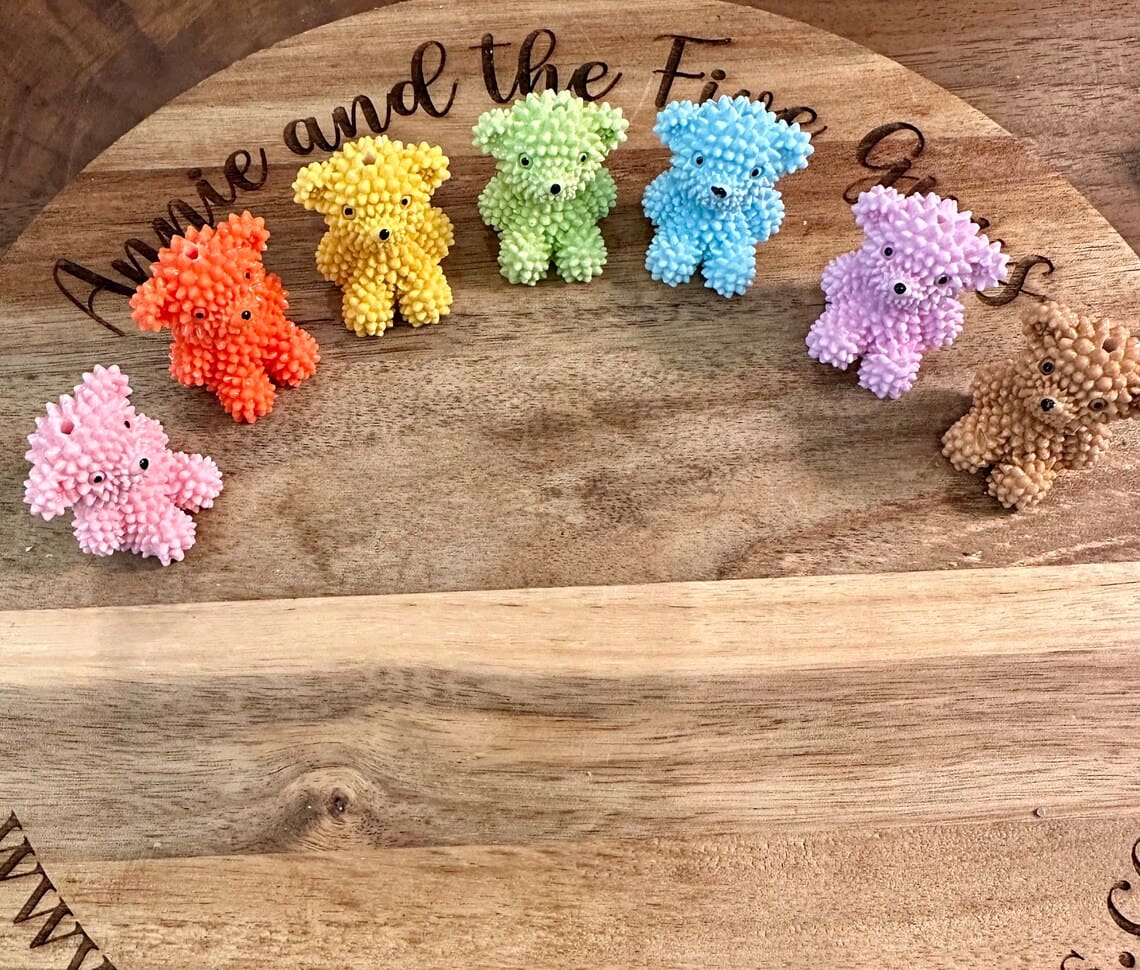 Six Bear furry looking acrylic beads in various colors (orange, pink, yellow, green, blue, purple, brown) are displayed on a wooden surface with text partially visible above.