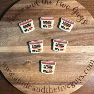 Five small pins resembling Ice cream silicone focal beads are placed on a round wooden surface with the text “Annie and the Five Guys” and a website address.