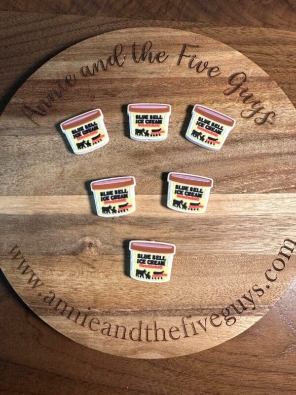 Five small pins resembling Ice cream silicone focal beads are placed on a round wooden surface with the text “Annie and the Five Guys” and a website address.