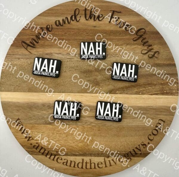 A round wooden board displays four rectangular Rosa Parks Silicone focal beads, each with the word "NAH." followed by "ROSA PARKS, 1955" printed in white text on a black background.