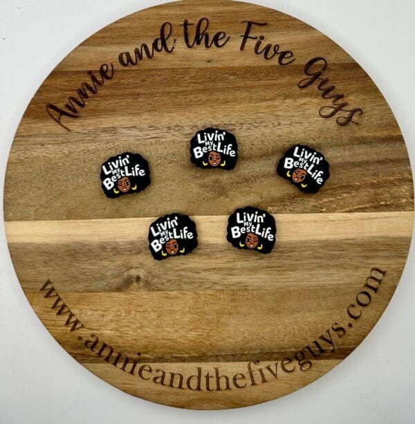 Five pins with the text "Livin' my Best Life" displayed on a round wooden board with the text "Annie and the Five Guys" around the edge.