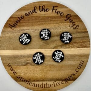 A wooden tray with "Annie and the Five Guys" engraved around the edge displays five round badges that read "Your anxiety is a lying hoe." The website "www.annieandthefiveguys.com" is also engraved.