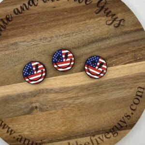 Three small, round pins with American flag designs are displayed on a wooden circular board with the text "www.annieandthefiveguys.com" around the edge.