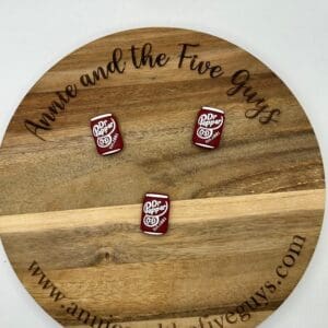 Round wooden board with the text "Annie and the Five Guys" and "www.annieandthefiveguys.com" engraved on it. Three small Dr pep silicone focal beads are placed on the board.