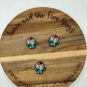 Three small, colorful gaming character pins are arranged on a wooden disc with the inscription "Annie and the Five Guys" and a website URL.