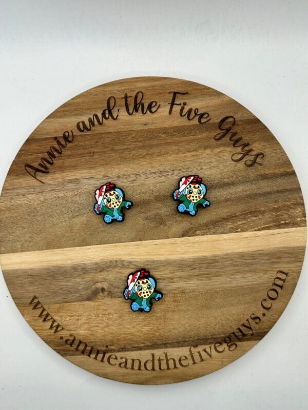 Three small, colorful gaming character pins are arranged on a wooden disc with the inscription "Annie and the Five Guys" and a website URL.