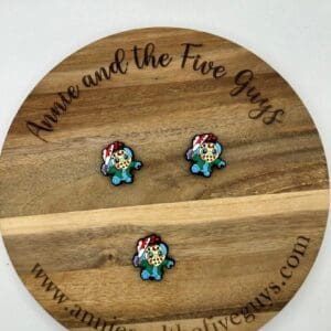 Three small, colorful gaming character pins are arranged on a wooden disc with the inscription "Annie and the Five Guys" and a website URL.