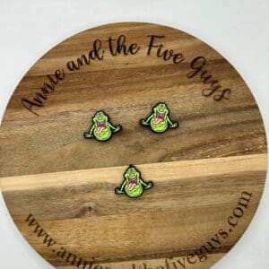 A round wooden board with the text "Annie and the Five Guys" and the website "www.annieandthefiveguys.com" displays three identical smiling cartoon character pins.