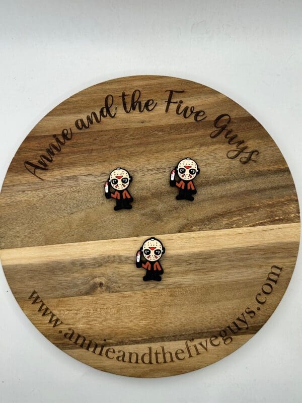 A wooden display board with the text "Annie and the Five Guys" showcases three small enamel pins depicting a cartoon character holding a knife. The website annieandthefiveguys.com is at the bottom.