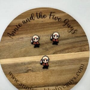 A wooden display board with the text "Annie and the Five Guys" showcases three small enamel pins depicting a cartoon character holding a knife. The website annieandthefiveguys.com is at the bottom.