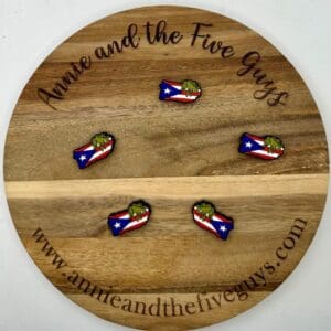 A wooden round sign reading "Annie and the Five Guys" with the website "www.annieandthefiveguys.com." It displays five small Puerto Rican Flag silicone focal beads featuring a green character over a flag design.