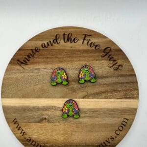 Three colorful, turtle-shaped items placed on a wooden circular board with the text "Anna and the Five Guys" and a website URL www.annaandthefiveguys.com.