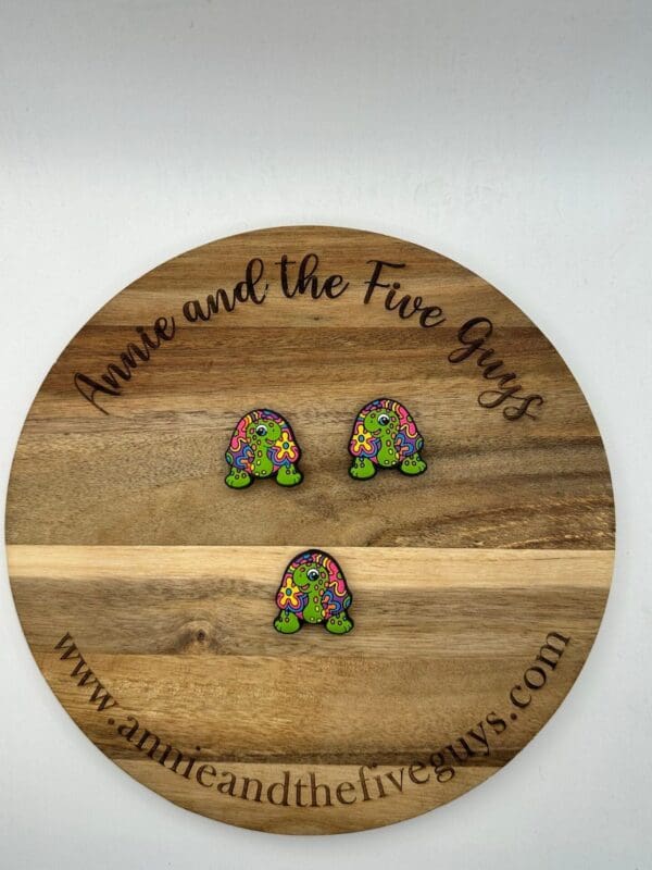 Three colorful, turtle-shaped items placed on a wooden circular board with the text "Anna and the Five Guys" and a website URL www.annaandthefiveguys.com.