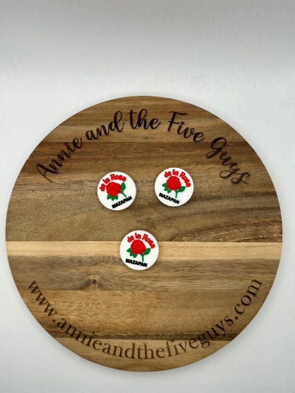 A wooden plaque with “Annie and the Five Guys” is engraved around its edge, displaying three round white pins, each with red and green designs and text reading "De La Rosa Mazapan.