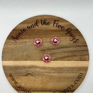 A wooden plaque displays three round pins with a panda logo. The plaque reads "Annie and the Five Guys" along with the website "www.annieandthefiveguys.com".