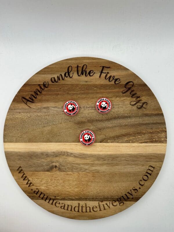 A wooden plaque displays three round pins with a panda logo. The plaque reads "Annie and the Five Guys" along with the website "www.annieandthefiveguys.com".