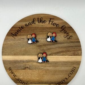 Chucky silicone focal bead with the text "Annie and the Five Guys" displaying three pins of two cartoon characters, a blonde girl and a red-haired boy, holding hands and facing forward.