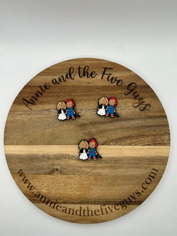 Chucky silicone focal bead with the text "Annie and the Five Guys" displaying three pins of two cartoon characters, a blonde girl and a red-haired boy, holding hands and facing forward.