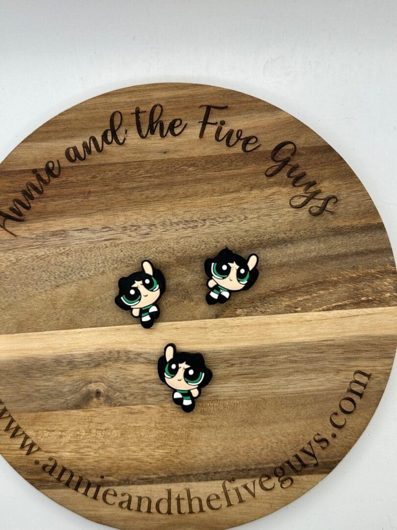 Three small character pins of Buttercup from The Powerpuff Girls placed on a round wooden board with text "anniceandthefiveguys.com" engraved around the edge.