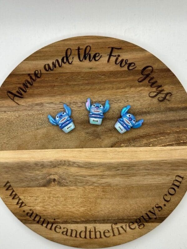 Three small, blue figurines with labels on a wooden tray that reads "Annie and the Five Guys" and has a web address at the bottom.