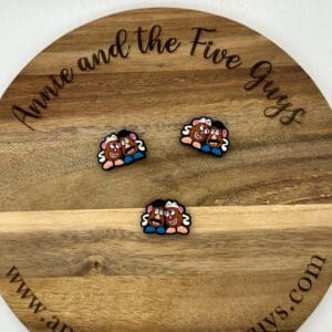 A wooden board engraved with "Annie and the Five Guys" featuring three small, cartoon-like pins resembling Mr. And Mrs. Potatoes Head silicone focal beads.