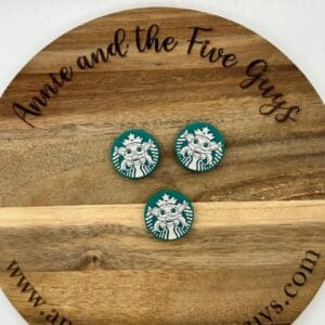 A wooden circular sign with the text "Annie and the Five Guys" features three Starbucks logo magnets placed in the center.