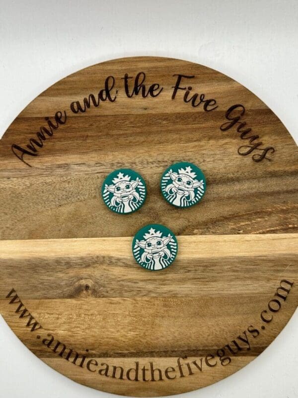 A wooden circular sign with the text "Annie and the Five Guys" features three Starbucks logo magnets placed in the center.