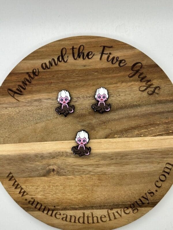 Three small pins featuring a character with white hair and purple skin are displayed on a wooden board with the text "Annie and the Five Guys.