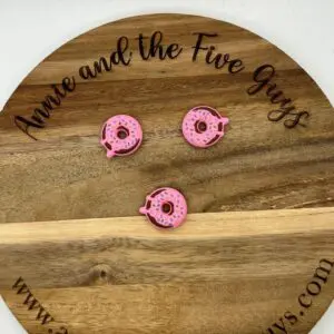 Three pink donut-shaped objects on a wooden board with the text "Annie and the Five Guys" and the website "www.annieandthefiveguys.com".