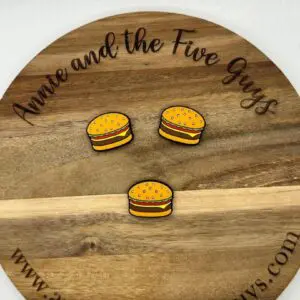 A wooden plaque with the text "Annie and the Five Guys" and "www.annieandthefiveguys.com" displays three cartoon-style burger magnets.