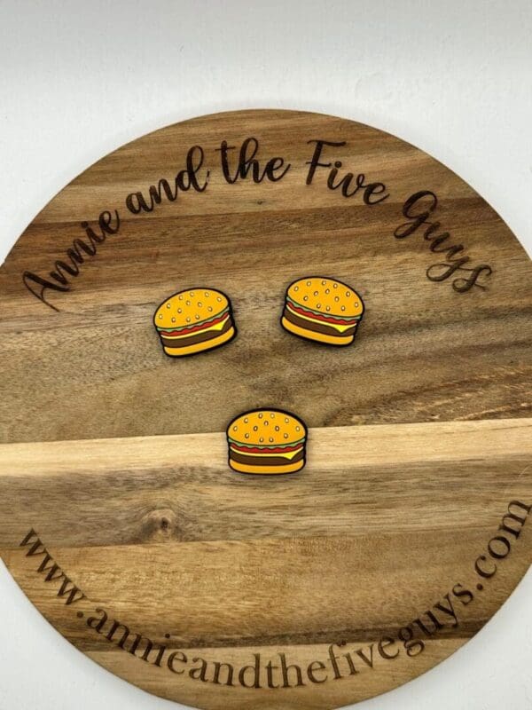 A wooden plaque with the text "Annie and the Five Guys" and "www.annieandthefiveguys.com" displays three cartoon-style burger magnets.