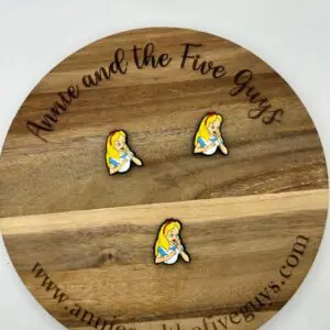 A circular wooden display with "Annie and the Five Guys" text holds three pins depicting a cartoon character with blonde hair and a blue dress. Website www.annieandthefiveguys.com is at the bottom.