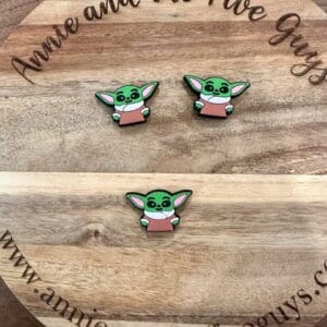 Three pins featuring a green character with large ears and wearing a pink shirt placed on a wooden circular board engraved with "Annie and the Five Guys" and a corresponding website URL.