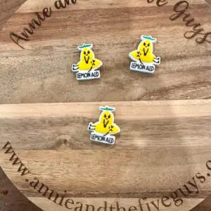 Three "Lemon Aid" stickers featuring a cartoon lemon with arms and legs are arranged on a wooden surface that reads "Annie and the Five Guys" around the edge.