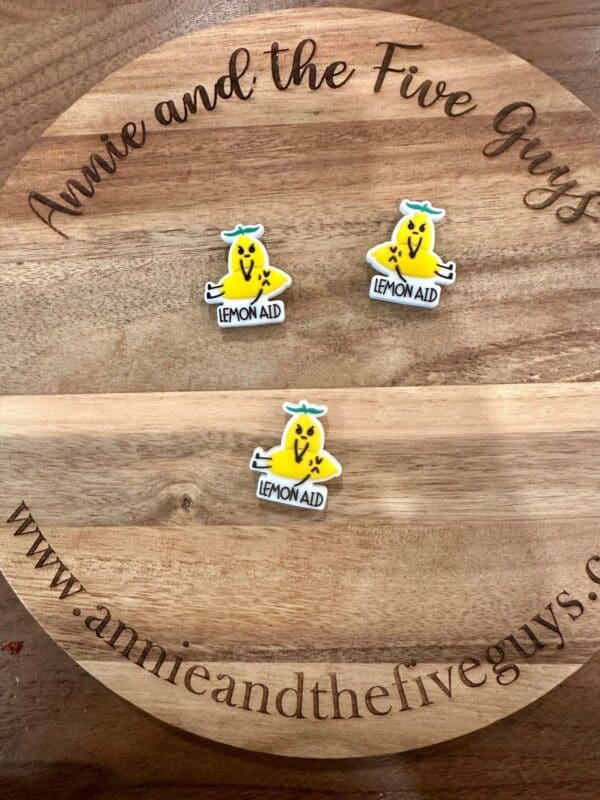 Three "Lemon Aid" stickers featuring a cartoon lemon with arms and legs are arranged on a wooden surface that reads "Annie and the Five Guys" around the edge.