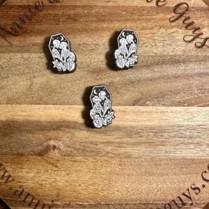 Three Kissing skeletons in a coffin silicone focal beads featuring white floral designs on a wood grain background with the text "Annie and the Five Guys.