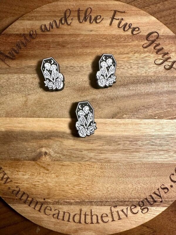 Three Kissing skeletons in a coffin silicone focal beads featuring white floral designs on a wood grain background with the text "Annie and the Five Guys.