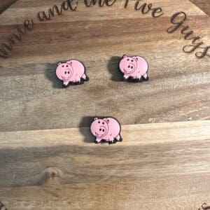 Three pink pig stickers laid out on a wooden surface with cursive text partially visible around the edge.